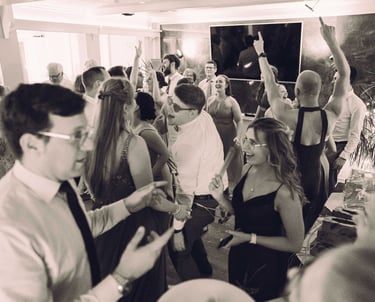 Ausgelassene Partygäste tanzen mit erhobenen Händen auf einer Hochzeitsfeier. Schwarz-Weiß-Foto von Joel Pingel.