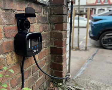 Black Ohme smart electric vehicle charger mounted on a brick wall for residential EV charging.