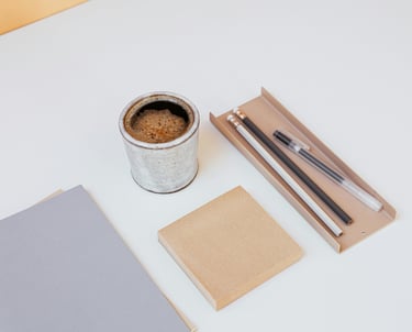 Minimalist desk workspace with a ceramic espresso cup, notebook, and stationery on a white surface.