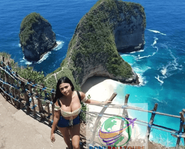 A woman stands overlooking Kelingking Beach in Nusa Penida, Bali with views of the iconic T-Rex cliff and turquoise water.