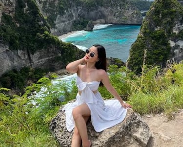 A woman in a white dress posing at Diamond Beach viewpoint in Nusa Penida, Bali.