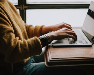 Photograph of a person sat at a desk with their hands on the keyboard of a laptop