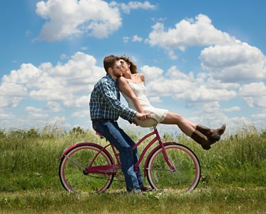 a man and woman riding a bicycle in the grass