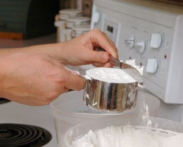 a person is holding a spoon and mixing a bowl of flour