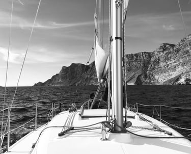 Black and white photo of the bow of a boat in the ocean in front of cliffs in good weather