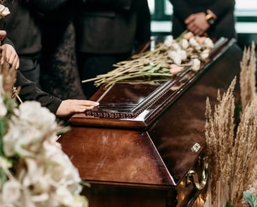 hand touching the dark brown stained coffin decorated by dried flowers