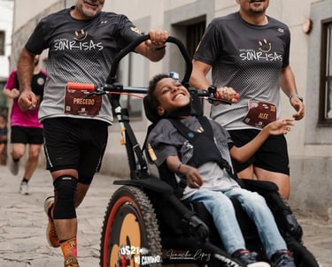 Dos hombres empujan corriendo una silla de ruedas adaptada donde se puede ver a un niño sonriendo