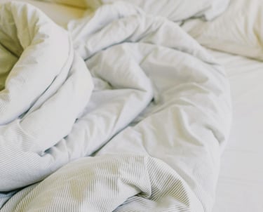 A bed that is not made up with a disheveled white duvet and four white pillows