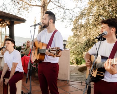 Live acoustic band with guitarists and a cajon player performing at an outdoor garden wedding reception.