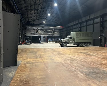 Vintage military airplane and army truck inside a large industrial hangar warehouse.