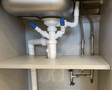 kitchen plumbing with a stainless steel sink drain, waste pipes, and flexible water supply pipes.