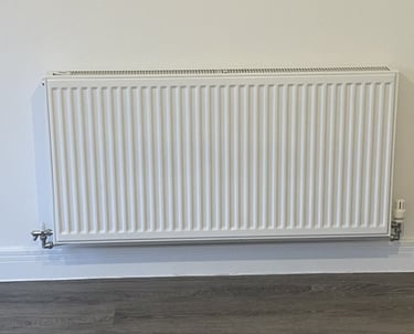 A modern white wall-mounted central heating radiator with a thermostat valve on a neutral wall.