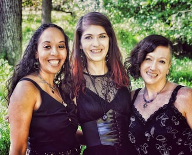 three women in black dresses standing in a forest