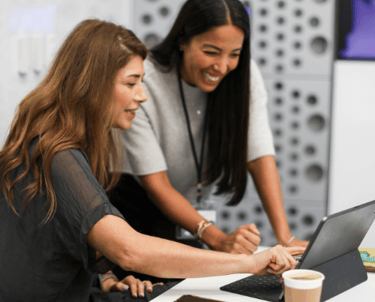 two women sitting at a table using an AI tool on a laptop
