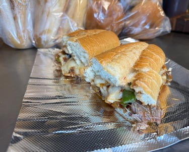 Texas-style brisket sandwich stacked with sautéed green peppers, onions, melted cheese, and drizzled