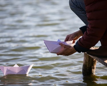 Bateau de papier flottant sur un lac, porteur d’un message symbolique d’adieu.