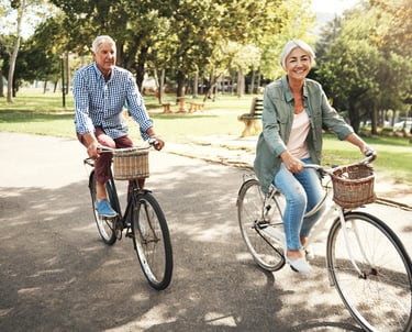 White haired woman and man ride bicycles next to park after treatment with acupuncture for pain