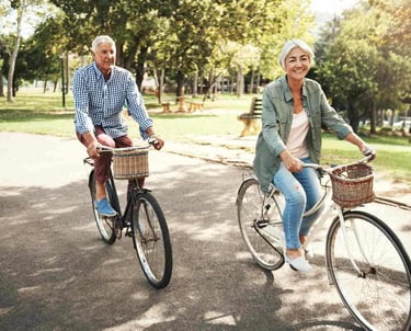 Older woman and man ride bicycles next to park after treatment with acupuncture for pain