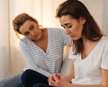 a woman sitting on a bed with her arm around a woman's neck
