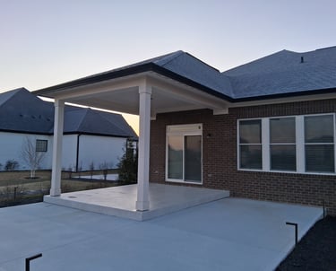 Covered patio with raised concrete floor under a roof with a larger uncovered concrete slab patio.