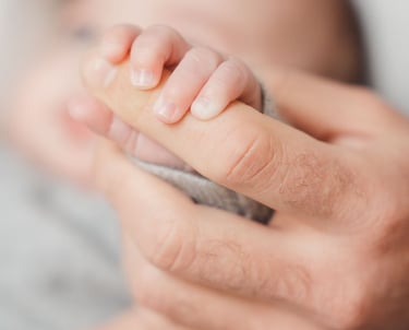Photographe naissance Paris : gros plan sur la main du bébé attrapant le doigt de son père