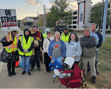 Large group of people standing with a on strike sign