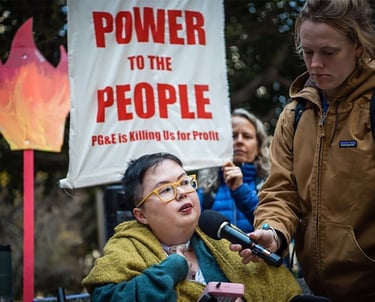 Photo of Stacey at a protest with sign that reads "power to the people PG&E is killing us for profit"