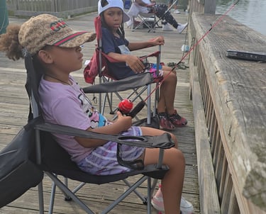 Two young girls sitting in folding chairs fishing from a wooden pier on a cloudy day.