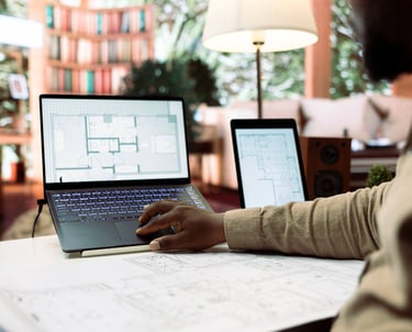 foto com foco laptop cm planta de arquitetura e  tablet ao lado e homem trabalhando sobre o projeto