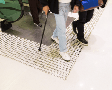 saida de escada rolante com piso tatil de alerta e pessoa com bengala circulando