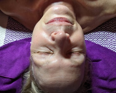 woman getting a facial with eyes closed on a purple towel