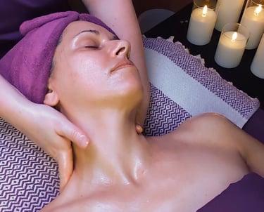A woman receives a relaxing facial massage at a spa with lit candles in the background.