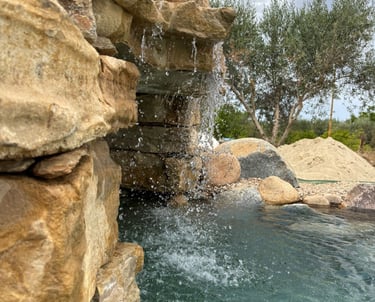 Piscina effetto spiaggia con cascata e area relax outdoor
