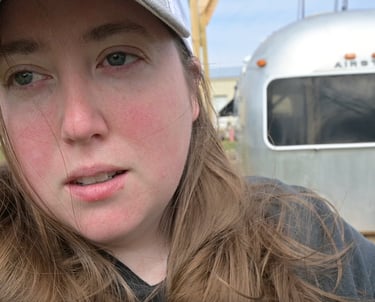 a woman in a hat standing in front of Airstream shell that is sitting on the ground