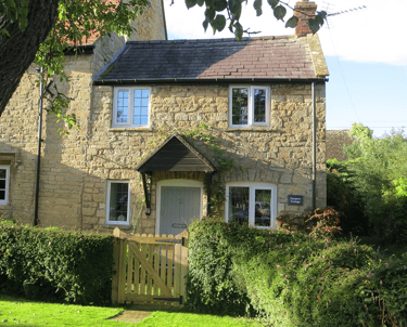 a photo of Campion Cottage, a small stone cottage in the sunshine with a lawned garden in the front