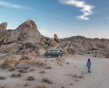 A rocky background with a van parked in the middle. A person seems to be walking towards the van.