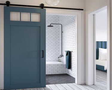 A modern blue sliding barn door with windows opening into a white subway tile bathroom with a black shower head.