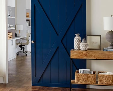 Modern navy blue sliding barn door with X-brace design leading to a home office.
