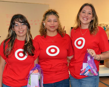 three women in red shirts are standing in a room holding hygiene kits