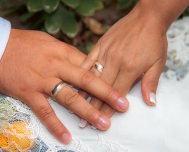 Primer plano de las manos de una pareja casada mostrando anillos de boda de oro sobre un vestido de 