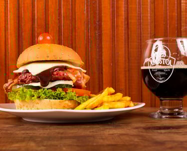 Hamburguesa gourmet con queso y tocino, patatas fritas y servida con un vaso de cerveza artesanal os