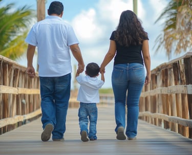 Fotografía de una madre y un padre tomando de cada extremo a su hijo pequeño caminando en un malecón