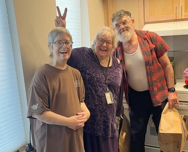3 seniors stand together in an empty kitchen smiling and posing for the camera