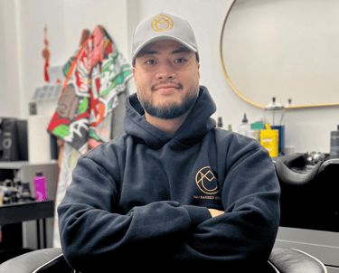 Yau, professional barber and founder of YAU Barber Studio, in his modern barber chair wearing branded hoodie and cap.