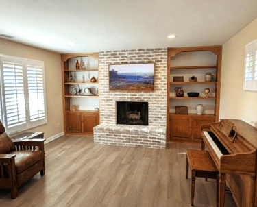 Living room with white brick fireplace, built-in wooden bookshelves, upright piano, and leather recliner.