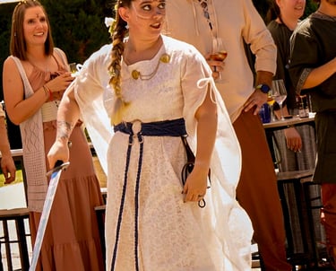 Mujer con vestido blanco y cinturón azul empuñando una espada durante una ceremonia de boda medieval