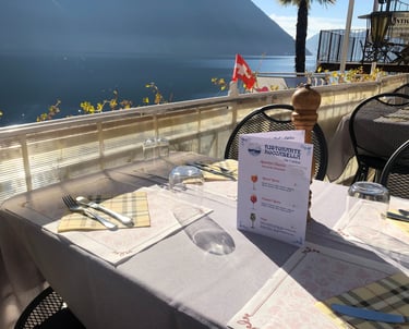 Un tavolo apparecchiato con vista sul lago di Lugano e un menu
