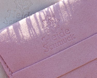 HeideSchmuck Schmuckverpackung aus edlem Samt in Rosa und Beige, fotografiert in der Heide mit blühendem Heidekraut.