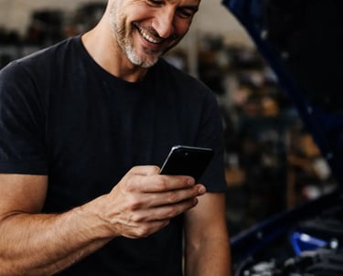 Meccanico sorride guardando lo smartphone, supporto Hulemex online che accompagna e spiega i prodott