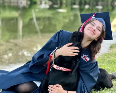 service dog in training nuzzles her puppy raiser who is wearing her cap and gown for senior pictures